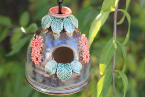 Small bird house, iridescent brown glaze with orange flowers and green leaves adorn this little home for our feathered friends. The leaves at the opening both serve as a perch and design. 